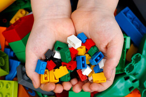 Tambov, Russian Federation - February 20, 2015 Lego Bricks in child's hands with Lego Duplo blocks and toys background. Studio shot.